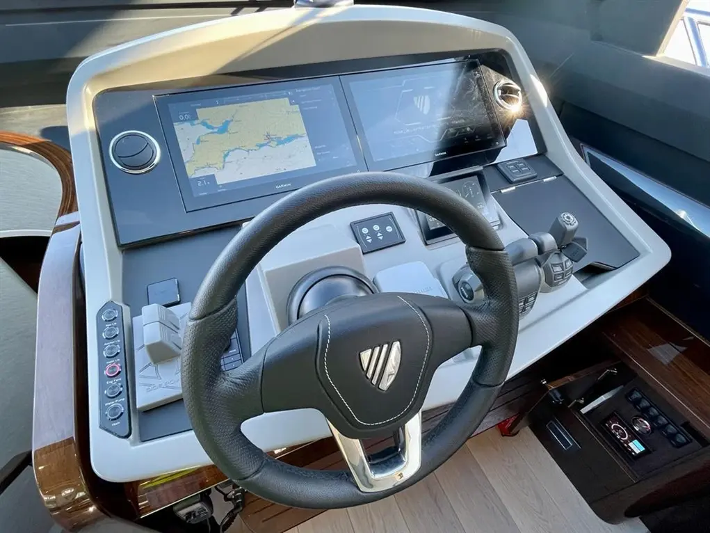 Yacht control panel featuring a steering wheel, navigational screens, and various control buttons. Garmin display visible.